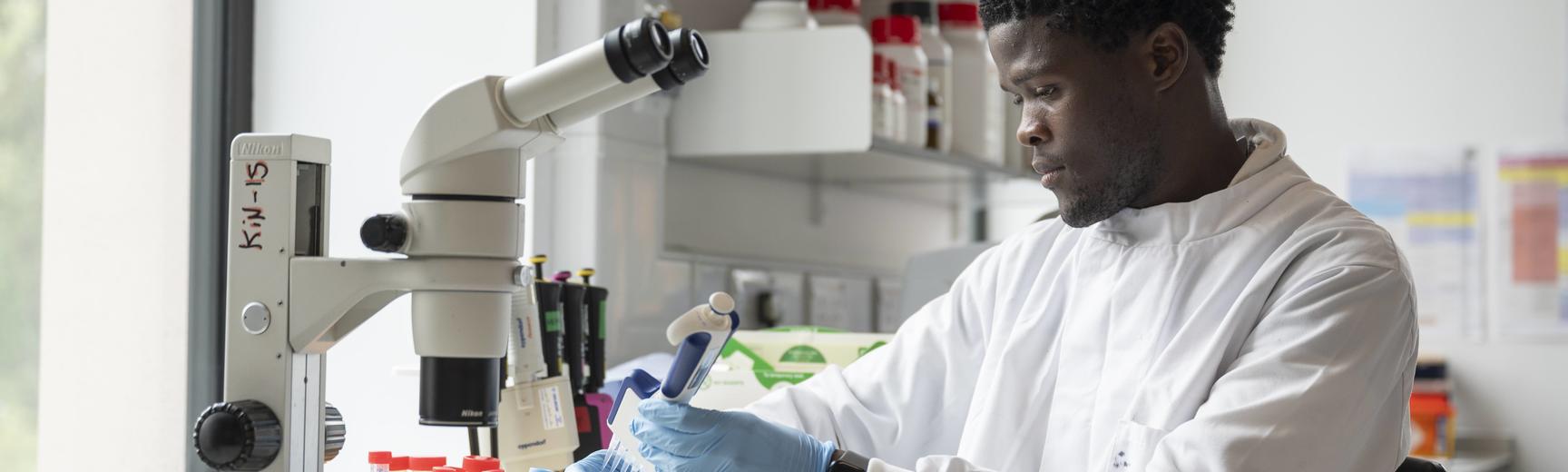 researcher sits in laboratory in a lab coat at a microscope