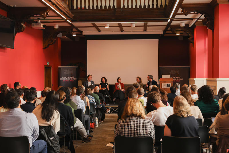 Panel discussion with five people sitting on a stage at the front of a room full of people