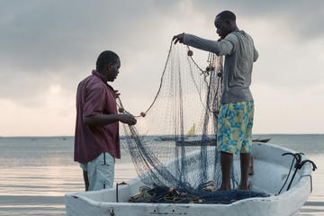 Two gillnet fishers stand on and beside a boat holding a net between them