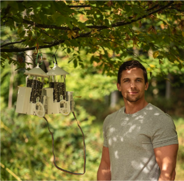 Dr Josh Firth standing in dappled light next to two smart bird feeders