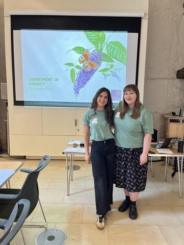Elsa and Isabelle stand in front of a screen wearing Department of Biology T.Shirts