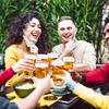 A group of people smile and cheers glasses of beer. All are lowering their face masks